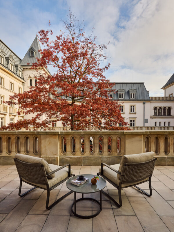 Two chairs and a small table on a balcony overlooking a tree with autumn foliage at The Florentin.