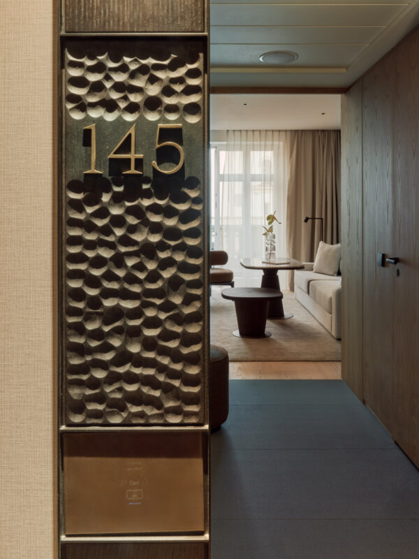 Room number 145 displayed on a textured door, leading to a modern hotel room with a seating area and natural light.