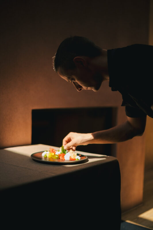 Chef Daniel Sanin carefully arranges colorful food on a plate in a softly lit setting.