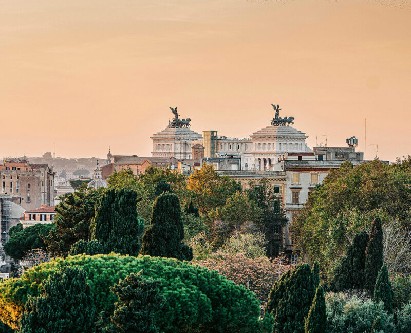 View of the Altare della Patria in Rome, framed by lush greenery and a warm sunset sky.