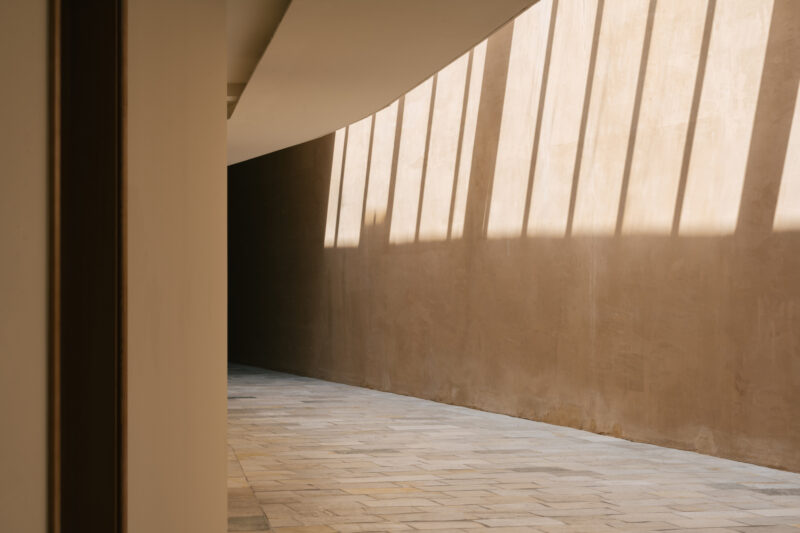 Sunlight casts shadows on a textured wall and floor in a minimalist interior space.