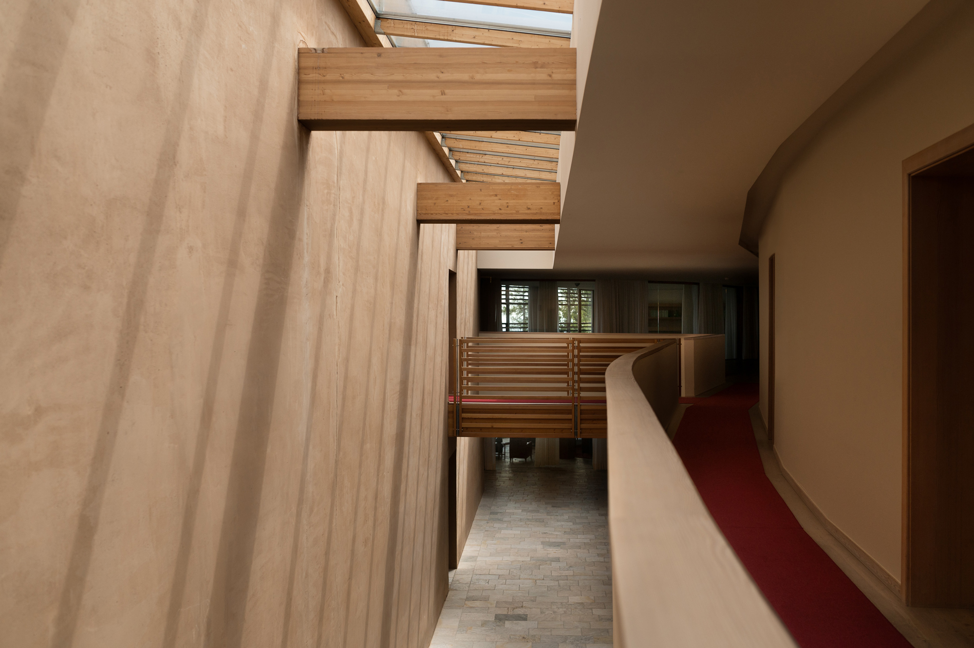 Interior view of a modern building featuring wooden beams, a curved railing, and natural light from a skylight.