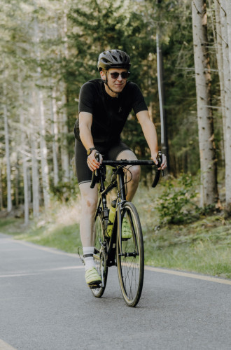 Cyclist in black attire riding a road bike on a tree-lined path near Parkhotel Mondschein.