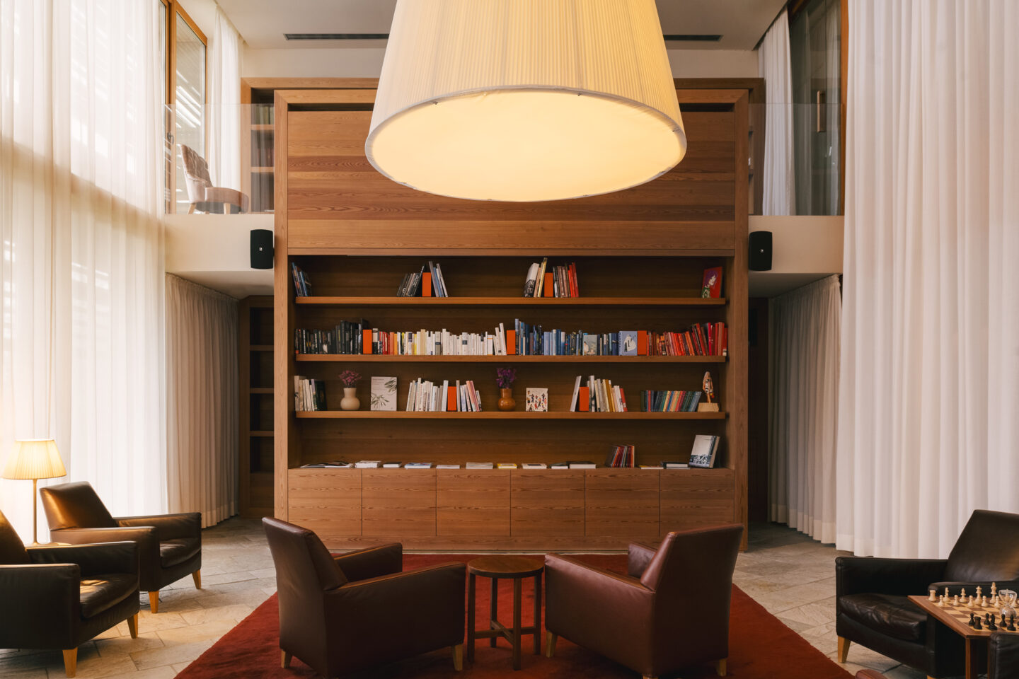 Cozy library with wooden shelves filled with books, two leather armchairs, a round table, and a large pendant light.