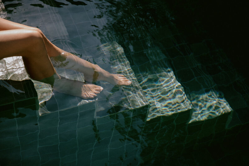 Feet submerged in a pool, with sunlight reflecting on the water's surface, creating a serene atmosphere.