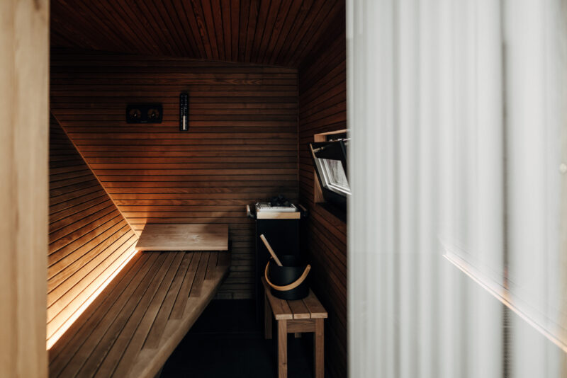 Wooden sauna interior with benches, ambient lighting, and a small shelf, partially obscured by a sheer curtain.