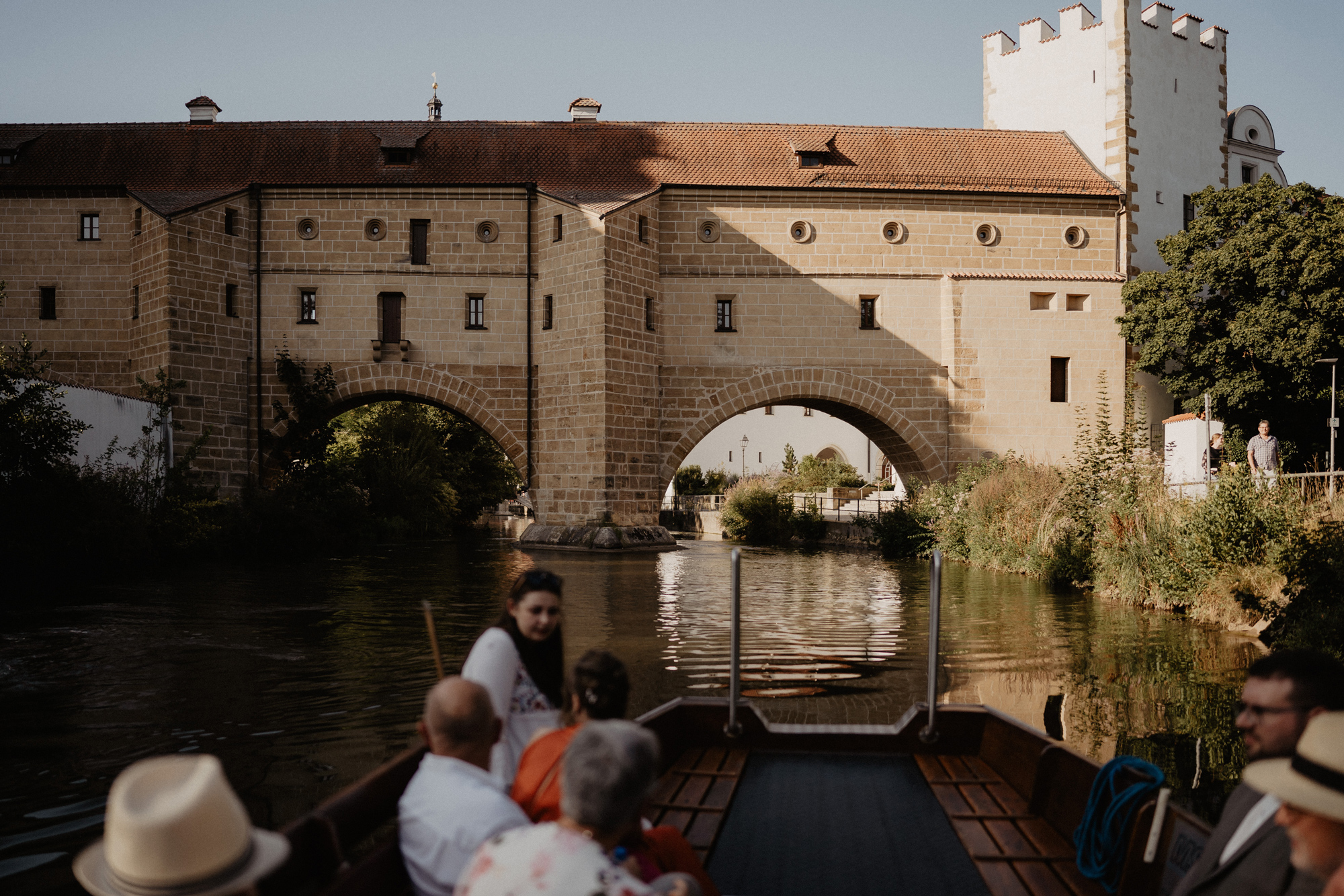 Scenic view of a historic stone bridge and building over a calm river, with people in a boat in the foreground.