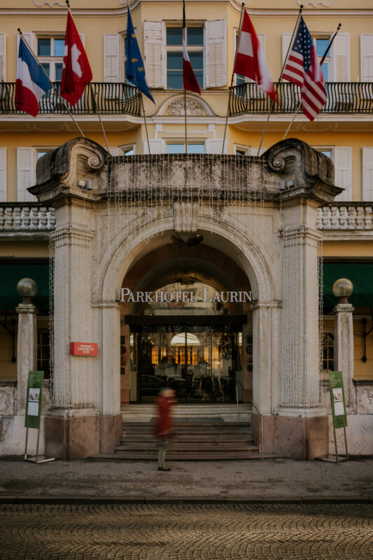 Entrance of Parkhotel Laurin with flags of Switzerland, EU, and the USA, and a blurred figure walking by.
