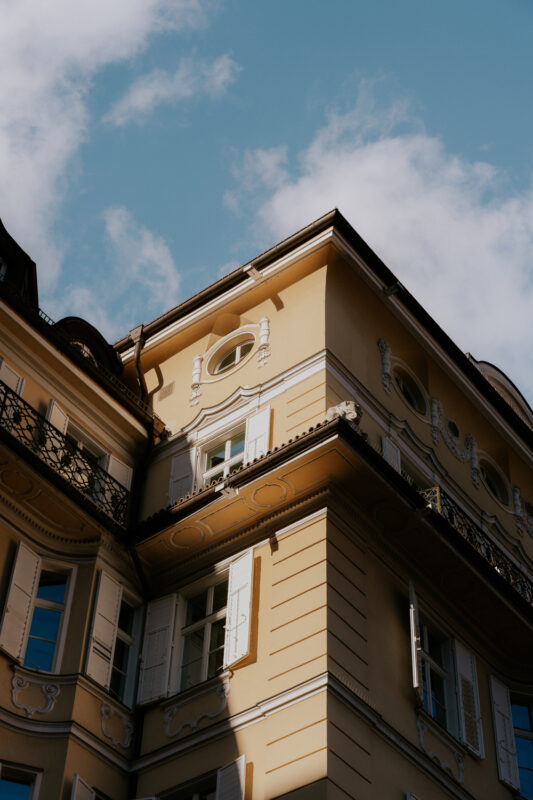 Corner view of a yellow building with ornate details and blue sky, uploaded to Parkhotel Laurin.