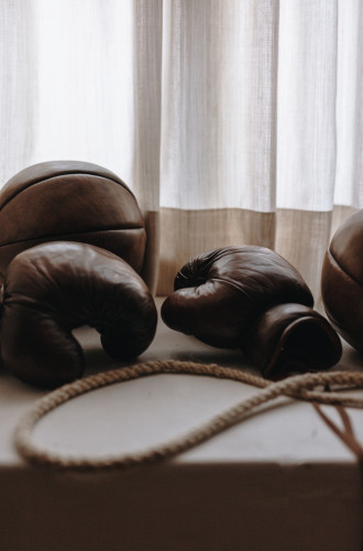 Brown leather boxing gloves and a rope resting on a ledge, with sheer curtains in the background.