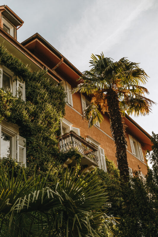 Historic building covered in greenery, featuring a balcony and palm trees, captured at Parkhotel Mondschein.