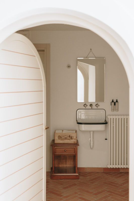 Bright bathroom with a sink, mirror, wooden cabinet, and radiator, framed by an arched doorway.