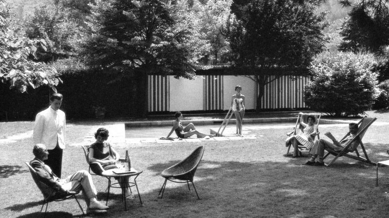 Guests relaxing in the garden of Parkhotel Laurin, featuring sunbathers, a pool, and lush greenery.