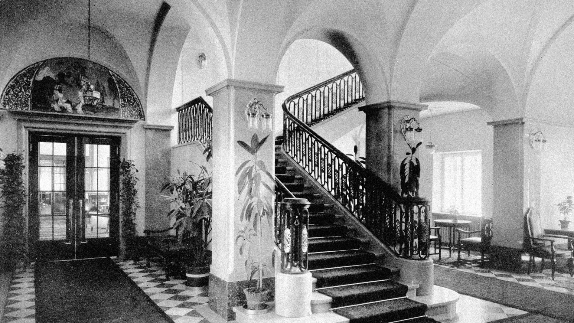 Elegant interior of Parkhotel Laurin featuring a grand staircase, arched ceilings, and decorative plants.