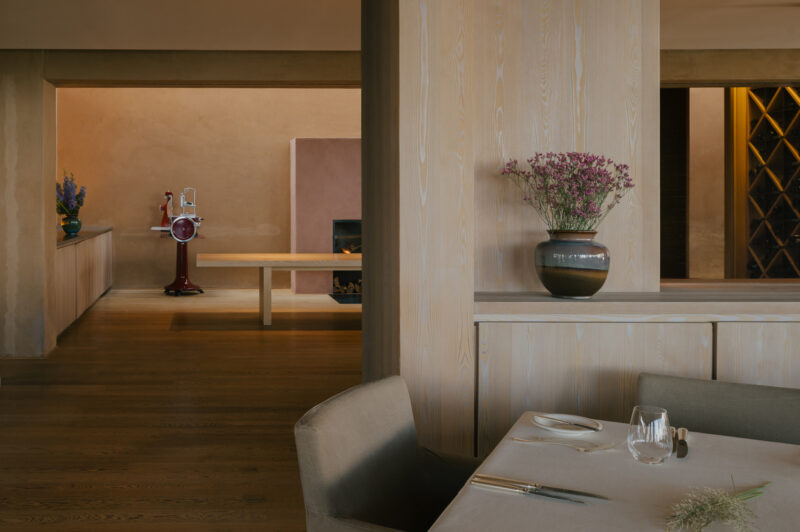 Modern restaurant interior featuring a wooden partition, a vase with flowers, and a glimpse of a fireplace.