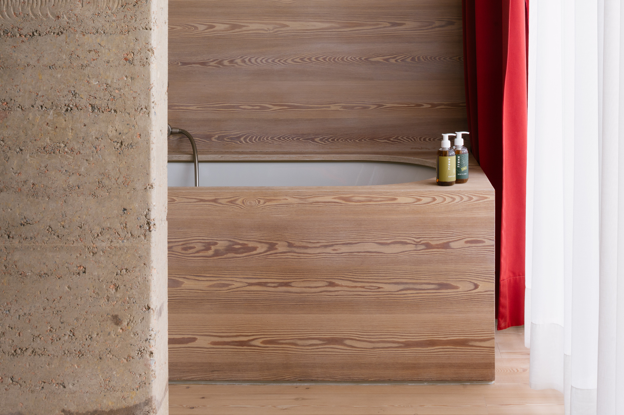 Wooden bathtub with a minimalist design, featuring natural wood paneling and red curtains, set in a modern room.