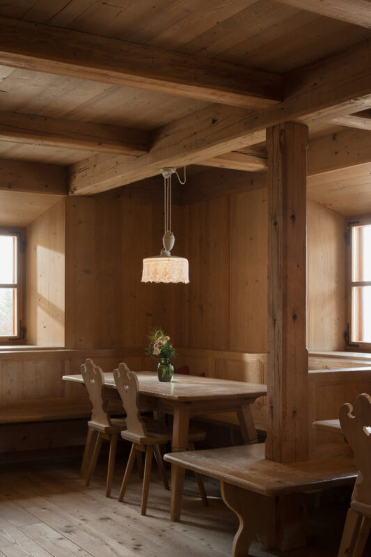 Wooden interior of a cozy room featuring a table, chairs, and a pendant light, with large windows letting in natural light.