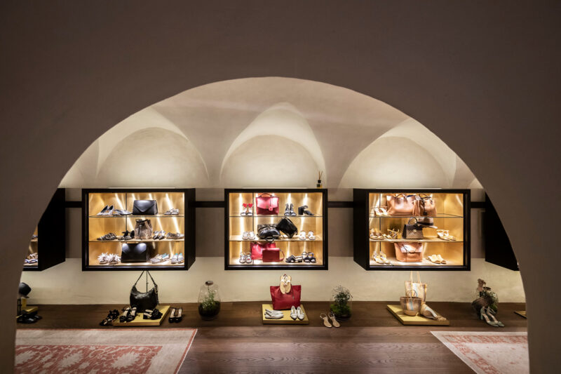 Elegant boutique display featuring shoes and handbags in illuminated shelves, set under arched ceilings.