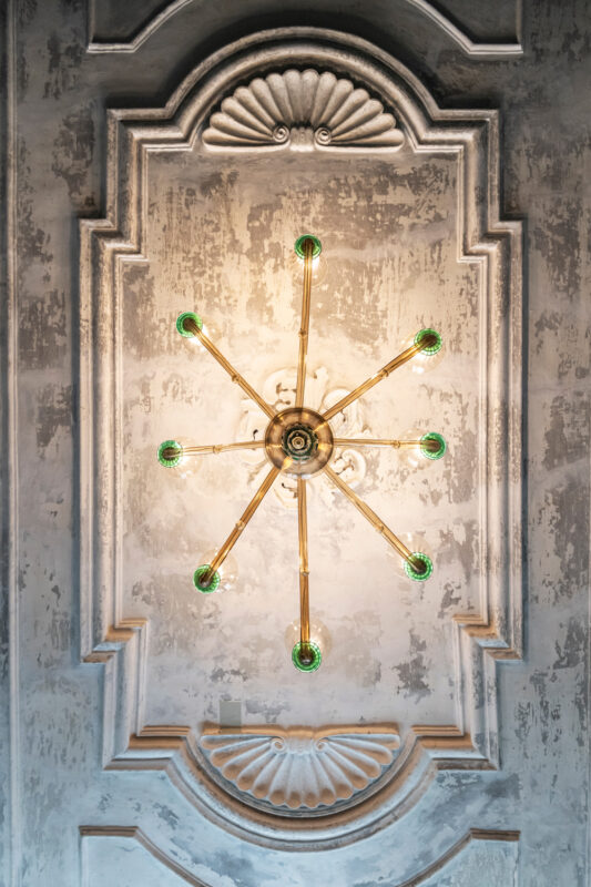 Chandelier with green bulbs hanging from a textured, ornate ceiling in a breakfast area.