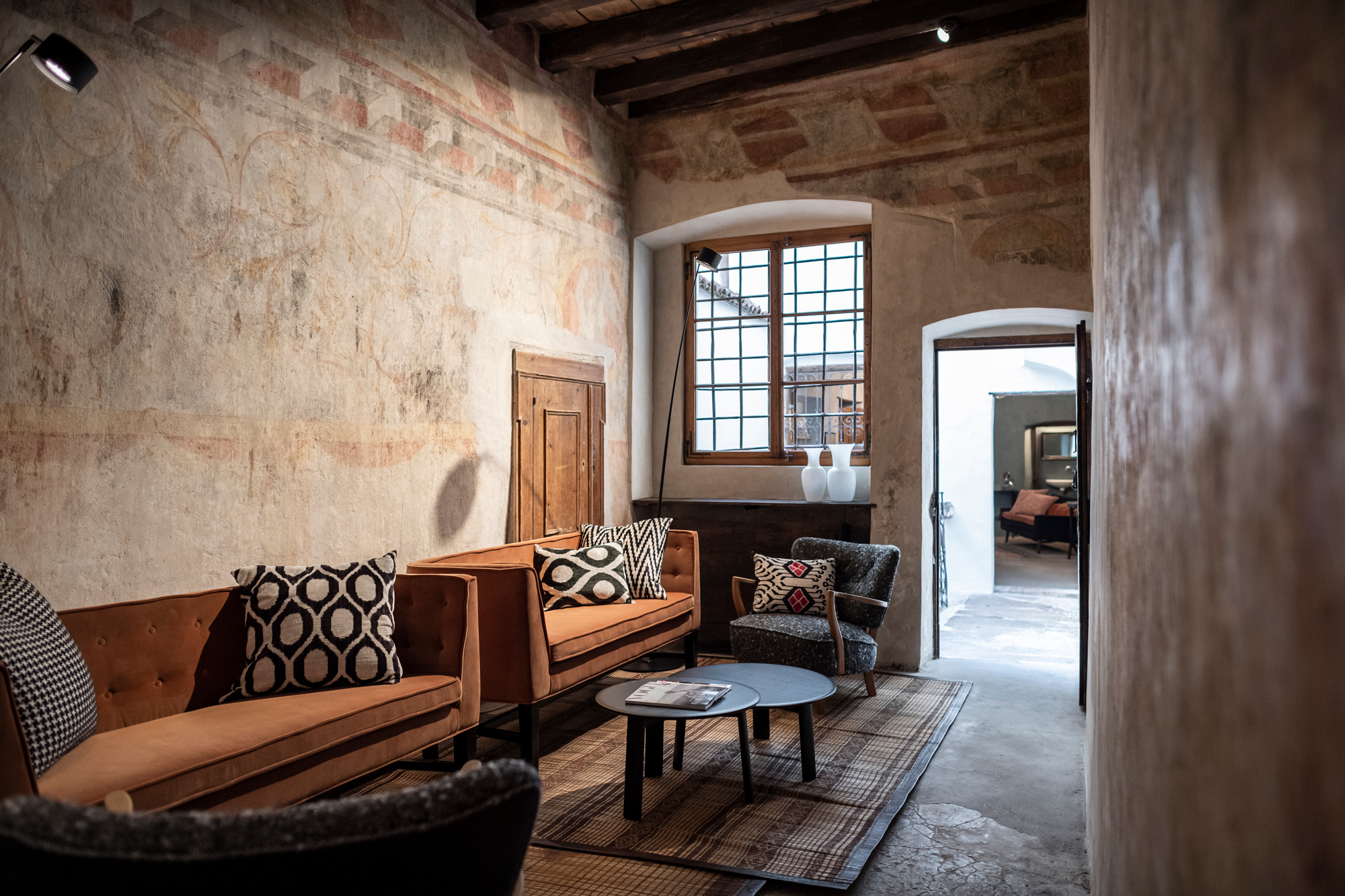 Cozy lobby with vintage furniture, patterned cushions, and a textured wall, featuring a doorway leading to another room.