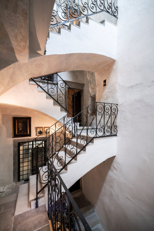 Elegant spiral staircase with ornate iron railings, leading to a doorway, framed artwork on the wall.