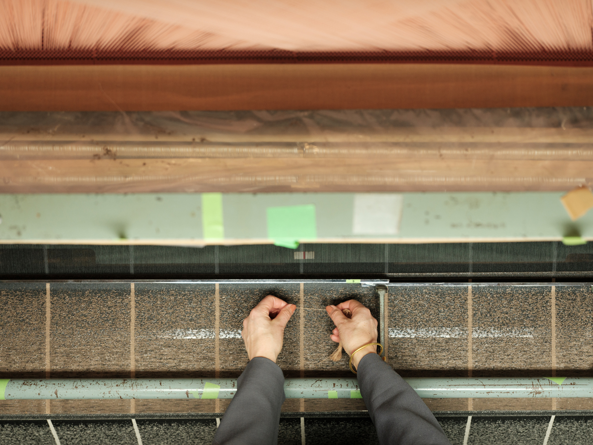 Hands adjusting a tile or panel along a horizontal surface, with a textured background and green tape visible.