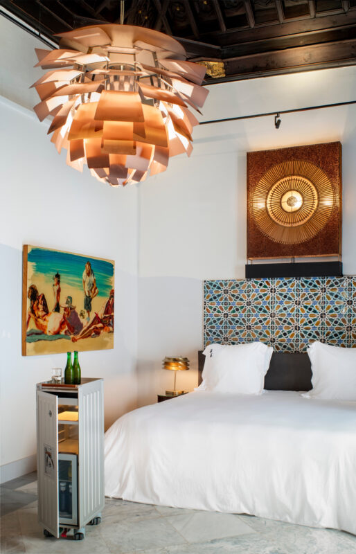 Stylish hotel room featuring a large bed, artistic wall decor, a unique light fixture, and a decorative tile backdrop.