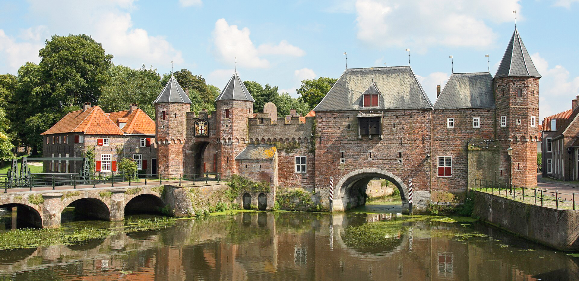 Koppelpoort, a historic brick gate with towers and a bridge surrounded by greenery.