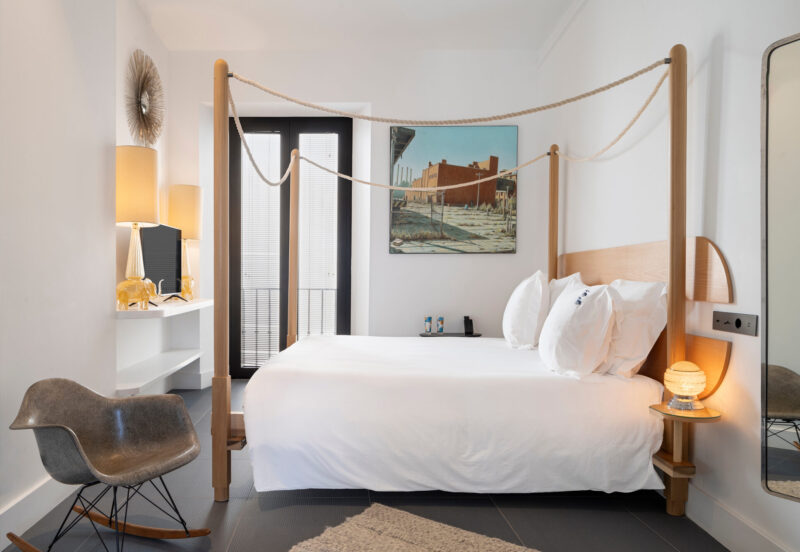 Modern hotel room featuring a four-poster bed, decorative artwork, and stylish furnishings.