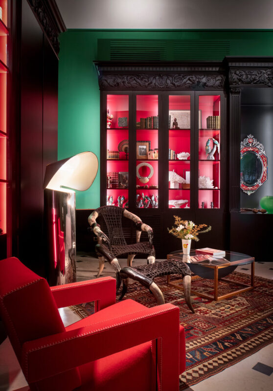 Stylish interior of Hotel Casa Limonero featuring red chairs, a decorative bookshelf, and a modern lamp against green walls.