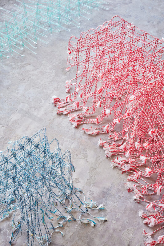 Colorful woven textile pieces in blue and red arranged on a textured surface, showcasing intricate patterns and fringes.