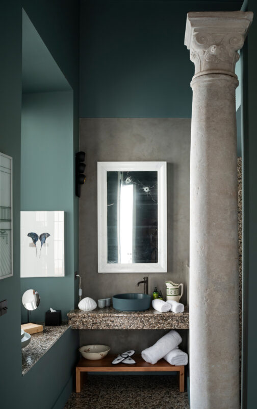 Modern bathroom featuring a stone column, a round basin, and a mirror, with towels and decorative items on a countertop.