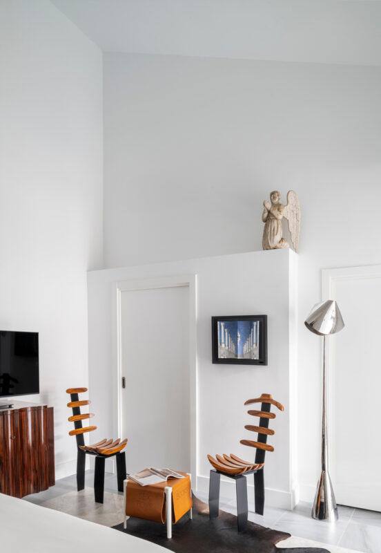 Modern hotel room featuring two unique wooden chairs, a sculpture of an angel, and a contemporary lamp.