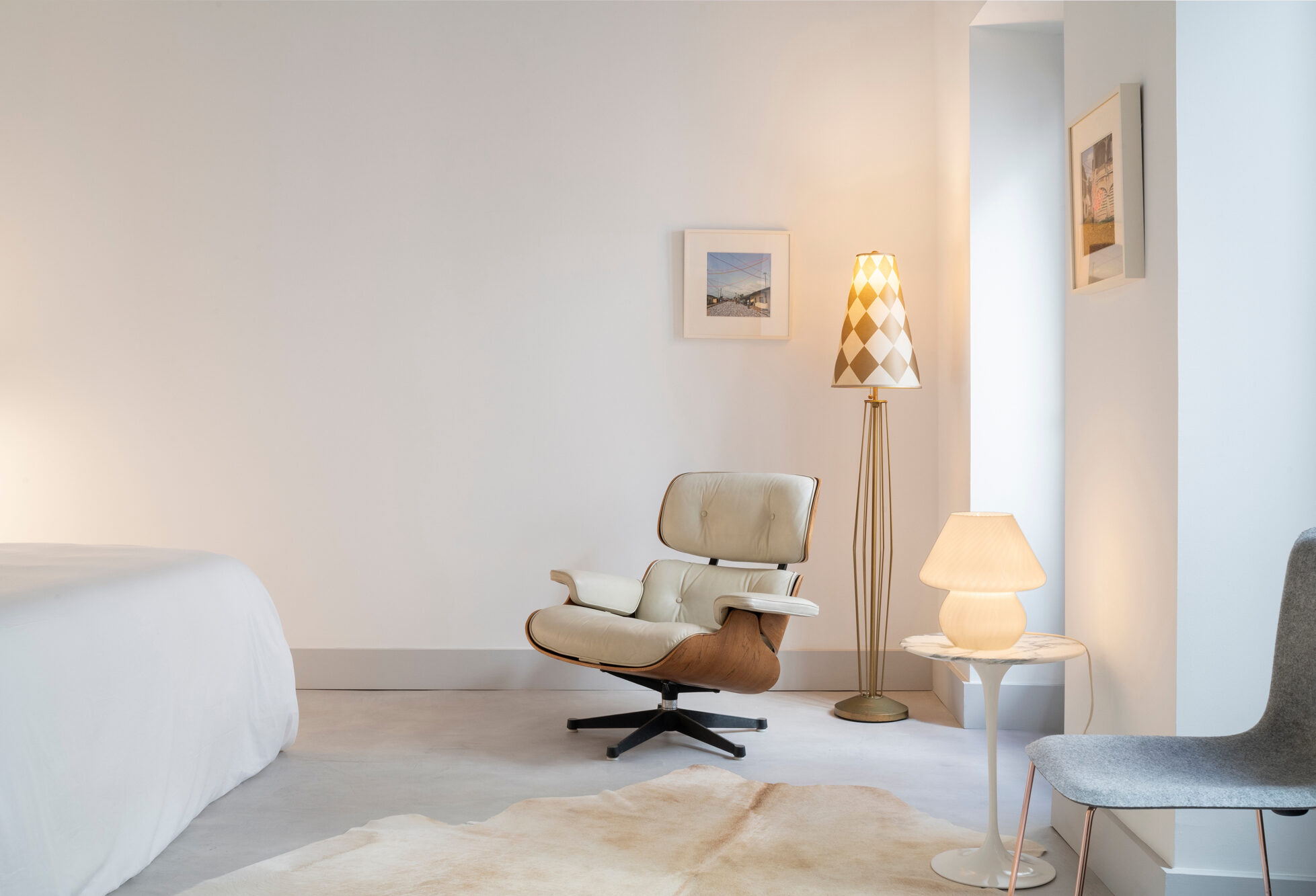 Modern hotel room featuring a stylish armchair, two lamps, and minimalist decor with artwork on the walls.