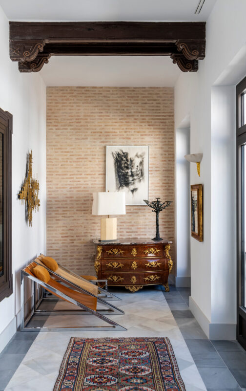 Elegant hallway in Hotel Casa Limonero featuring a vintage chest, modern chairs, a lamp, and decorative wall art.