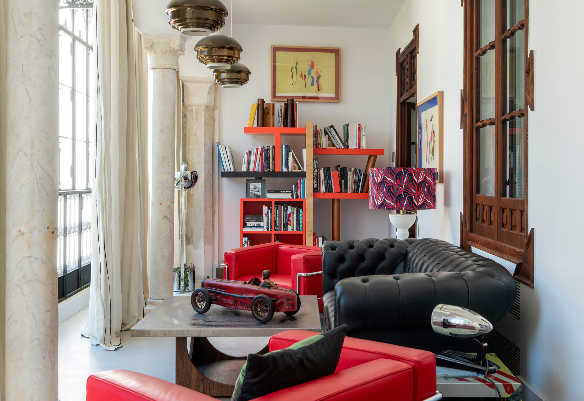 Modern living room featuring a black tufted sofa, red chairs, a bookshelf with books, and decorative items.