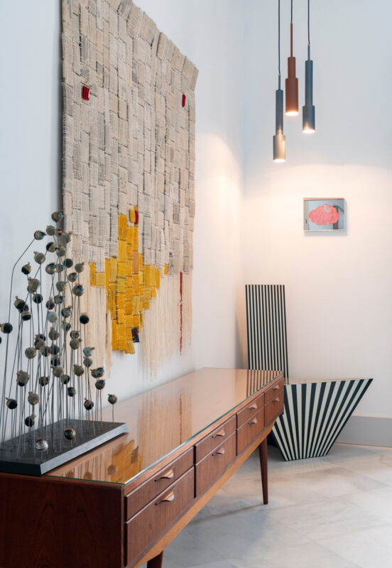 Modern interior featuring a wooden sideboard, abstract wall art, pendant lights, and a striped decorative object.