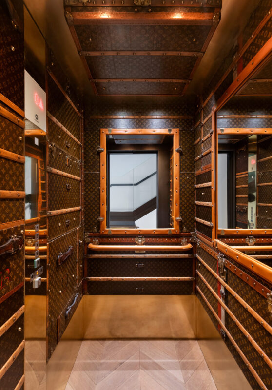 Luxurious elevator interior with patterned walls, wooden accents, and a large window showcasing a staircase.