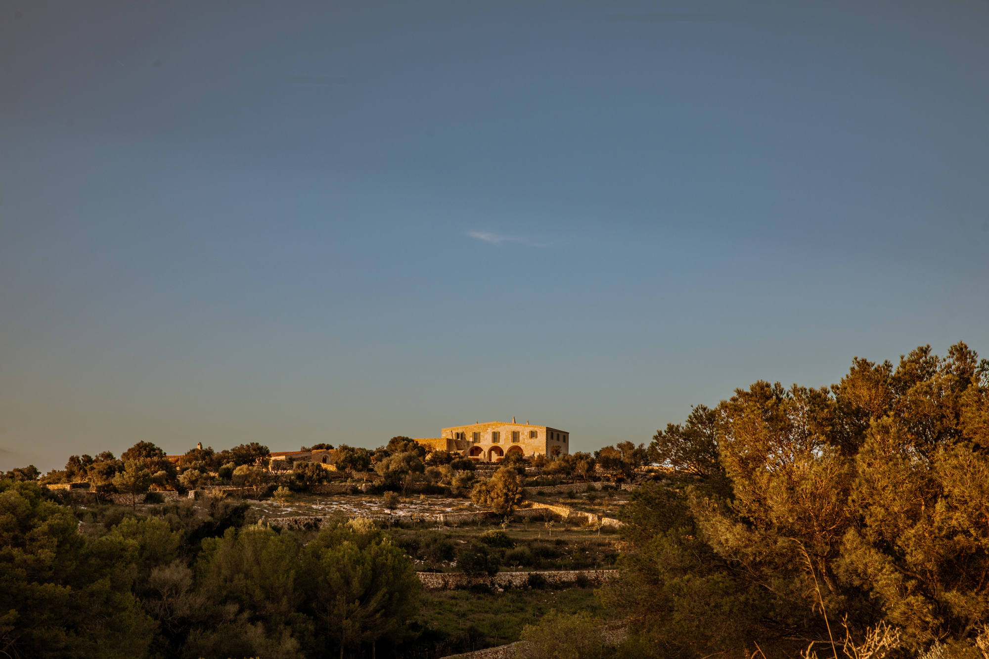 Historic building on a hilltop surrounded by trees under a clear sky, captured in Son Blanc, Menorca.