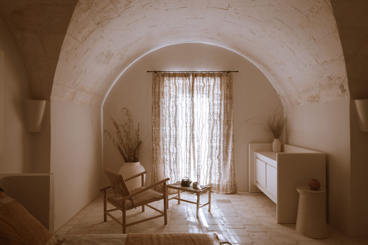 Cozy interior of a room with arched ceiling, natural light filtering through sheer curtains, and minimalist furniture.