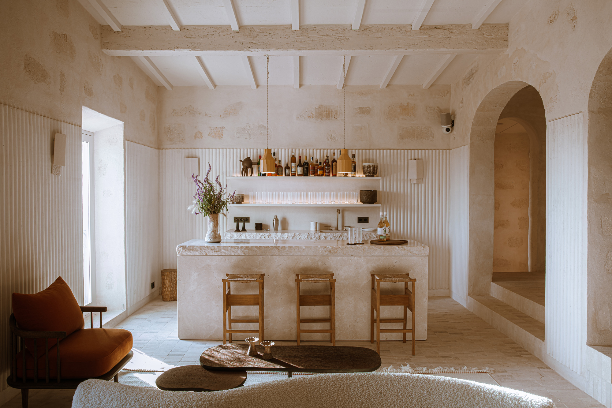 Modern interior of a light-filled space featuring a minimalist bar, wooden stools, and elegant decor.