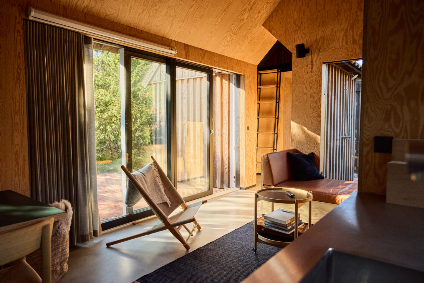 Bright interior of a cozy cabin with large windows, a wooden chair, and a sofa, surrounded by natural light.