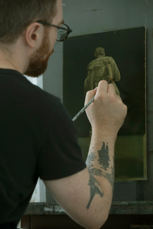 Artist with a tattoo painting a classical sculpture on a canvas, in a studio setting.