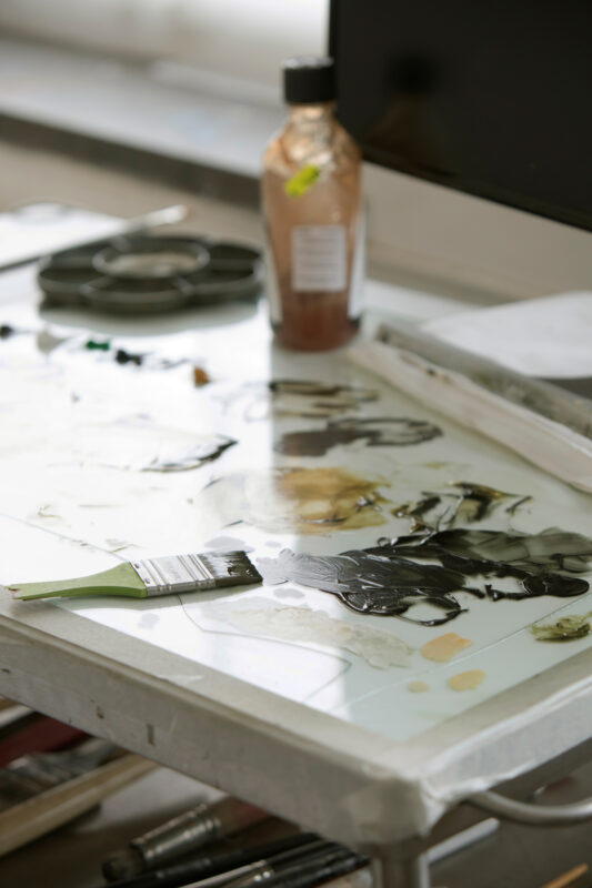 Palette with mixed paints and a brush on a work surface, with a bottle of paint visible in the background.