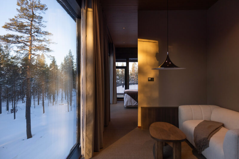 Cozy hotel room with a white sofa and wooden table, large window showcasing snowy trees outside at Gáldu Hotel & Spa.