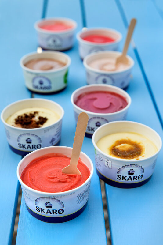 Colorful ice cream cups in various flavors arranged on a blue table, with wooden spoons in some cups.