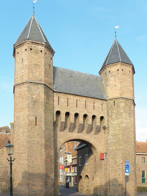 Historic brick gate with two towers, known as Kamperbinnenpoort, in Amersfoort, under a clear blue sky.