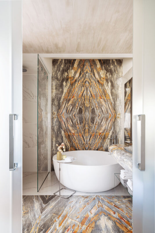 Luxurious bathroom featuring a freestanding tub, marble walls with orange and gray patterns, and a glass shower.