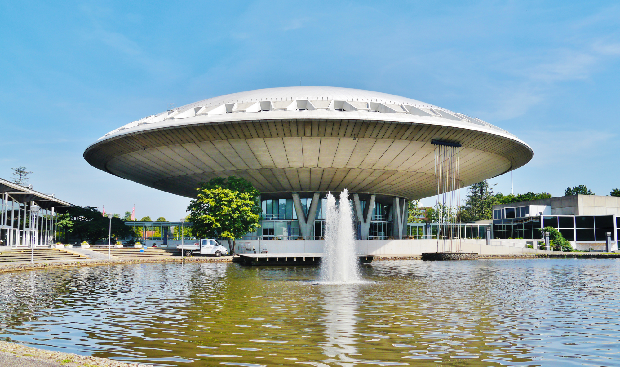 Evoluon building in Eindhoven, featuring a futuristic design, surrounded by water and greenery under a clear blue sky.