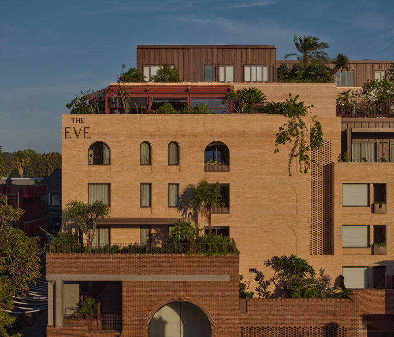 Modern building exterior of The EVE Hotel Sydney, featuring greenery and architectural details against a blue sky.